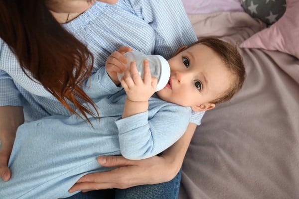 bébé tenant son biberon